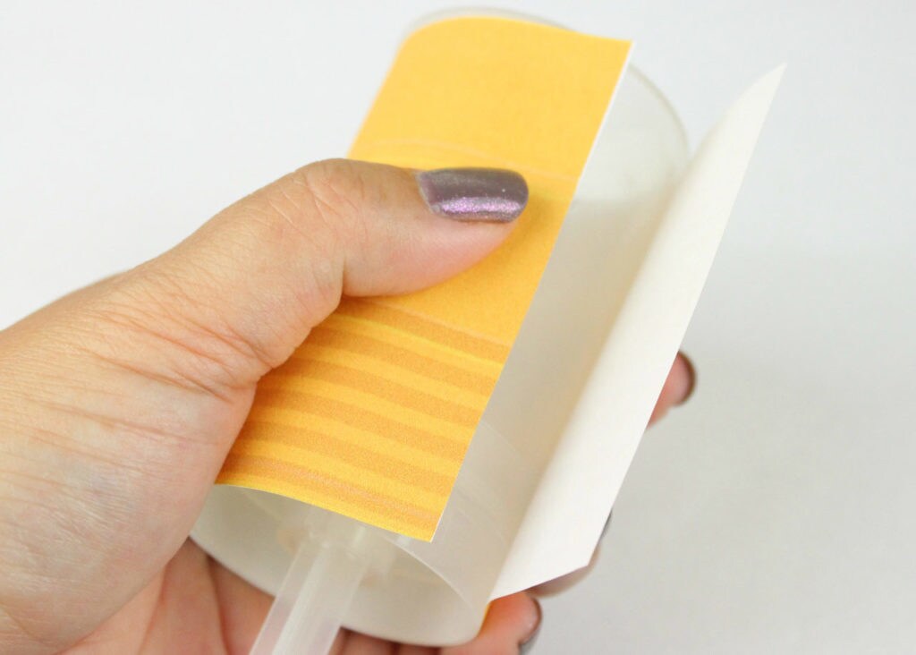 A push pop container is covered with yellow and orange stripped paper.