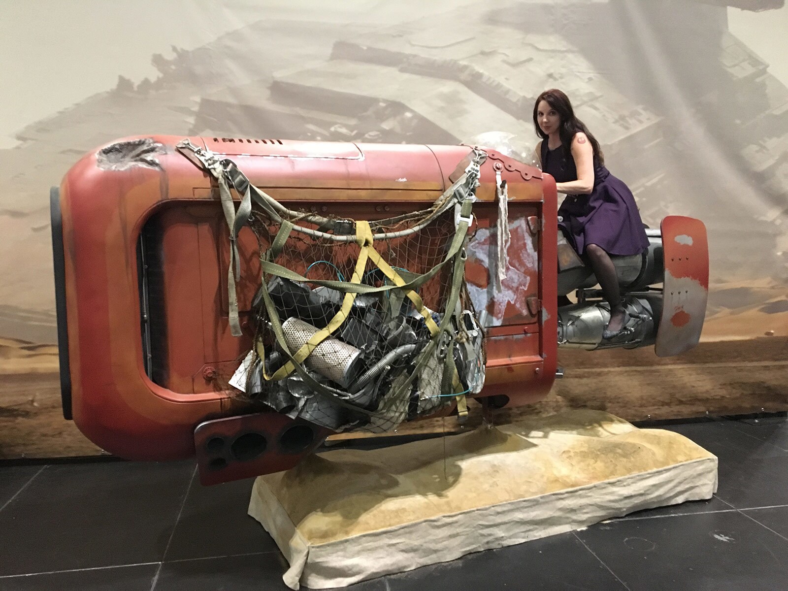 A fan poses on a model of Rey's speeder from The Force Awakens.