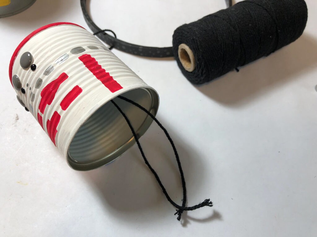 A tin can, painted to look like R5-D4, lies on its side with string attached, next to a spool of black string.