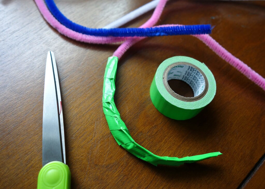 Pipe cleaners wrapped in duct tape sit on a table with a pair of scissors.