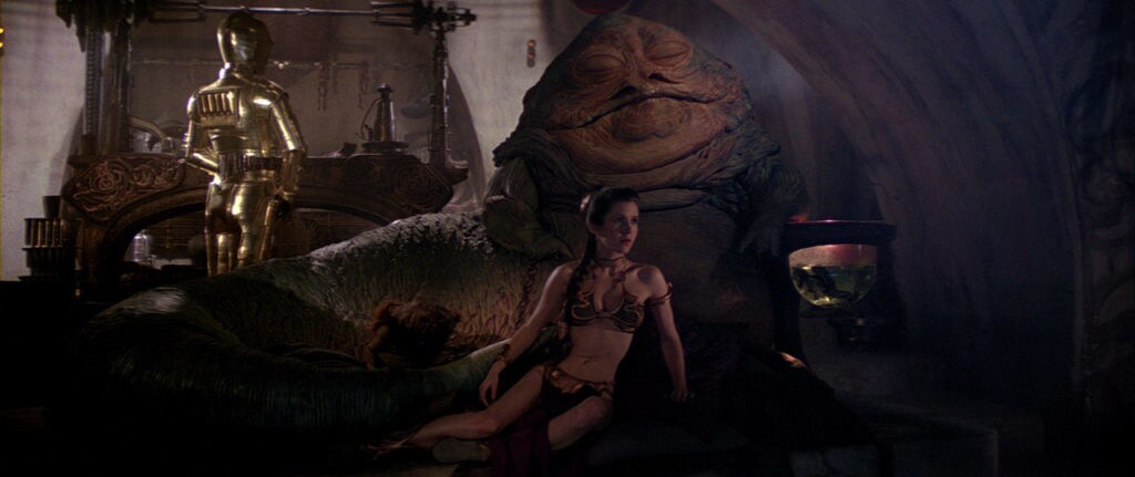 Princess Leia, in her iconic golden bikini, lounges in front of a sleeping Jabba while C-3PO stands nearby in Return of the Jedi.