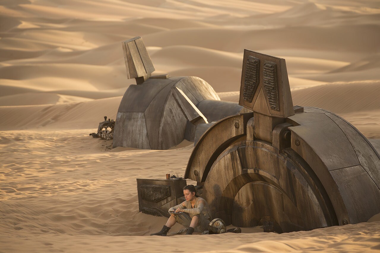 Rey sits next to wreckage on Jakku in Star Wars: The Force Awakens.