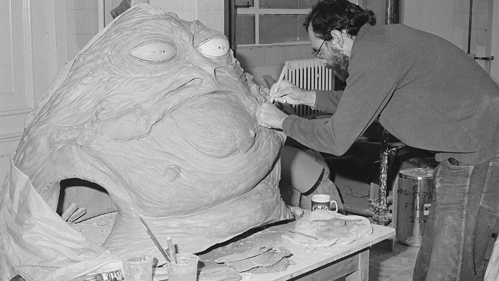 A prop designer sculpts a Jabba the Hutt model in his workshop.