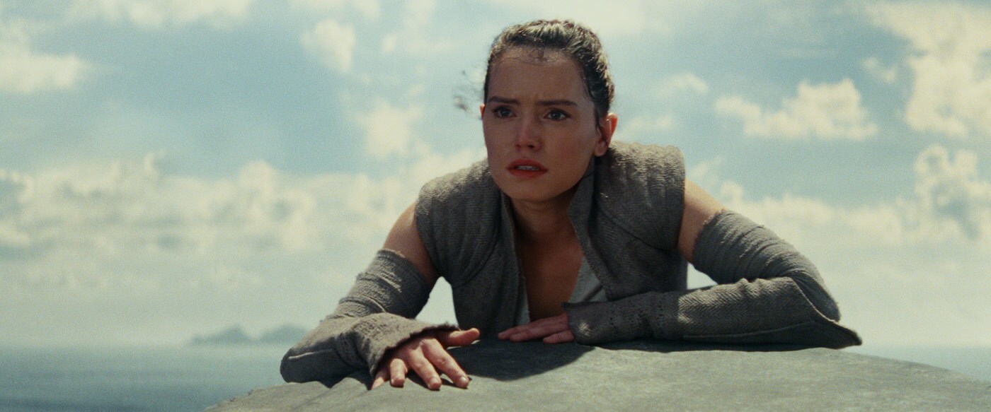 Rey climbs over the edge of a large rock in The Last Jedi.