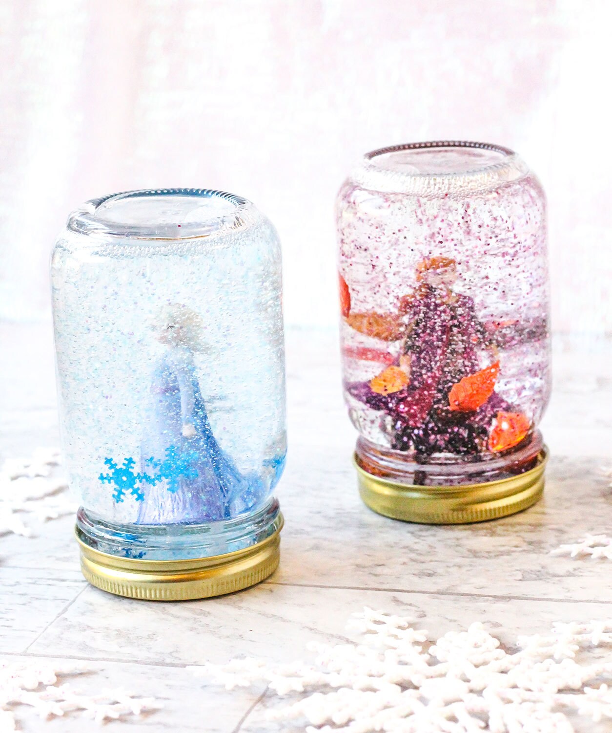 Two Frozen II-inspired snow globes filled with glitter. One snow globe has Elsa and blue snowflake sequins inside, and the other features Anna and orange leaf sequins.