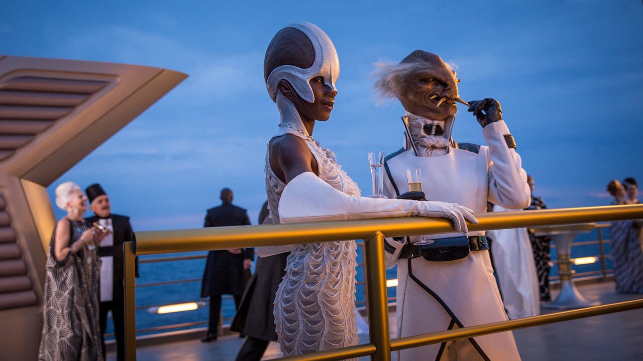 Baron Yasto Attsmun and Ubialla Gheal stand on the deck of the baron's yacht while guests mingle in the background in The Last Jedi.