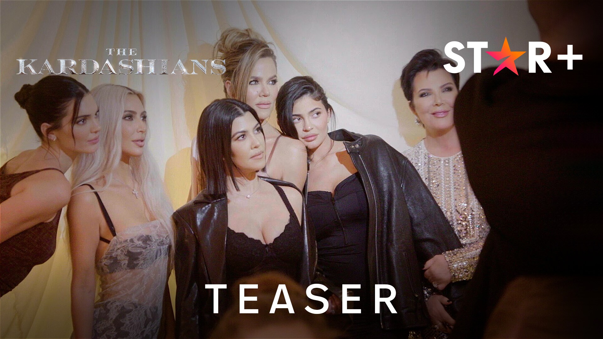 Kourtney Kardashian, Kim Kardashian, Khloe Kardashian and Kris Jenner stand next to each other looking to the left of the image, the shot features mostly their faces. 'The Kardashians' title is in the top left of the image, the 'Disney+' logo is in the top right and 'Official Trailer' is in the foreground.