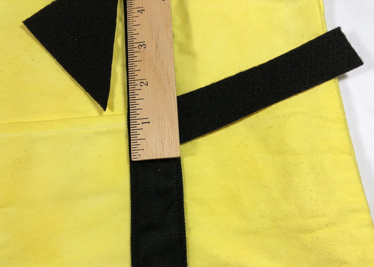 A strip of black felt the width of a ruler, next to a black felt triangle on top of yellow canvas.