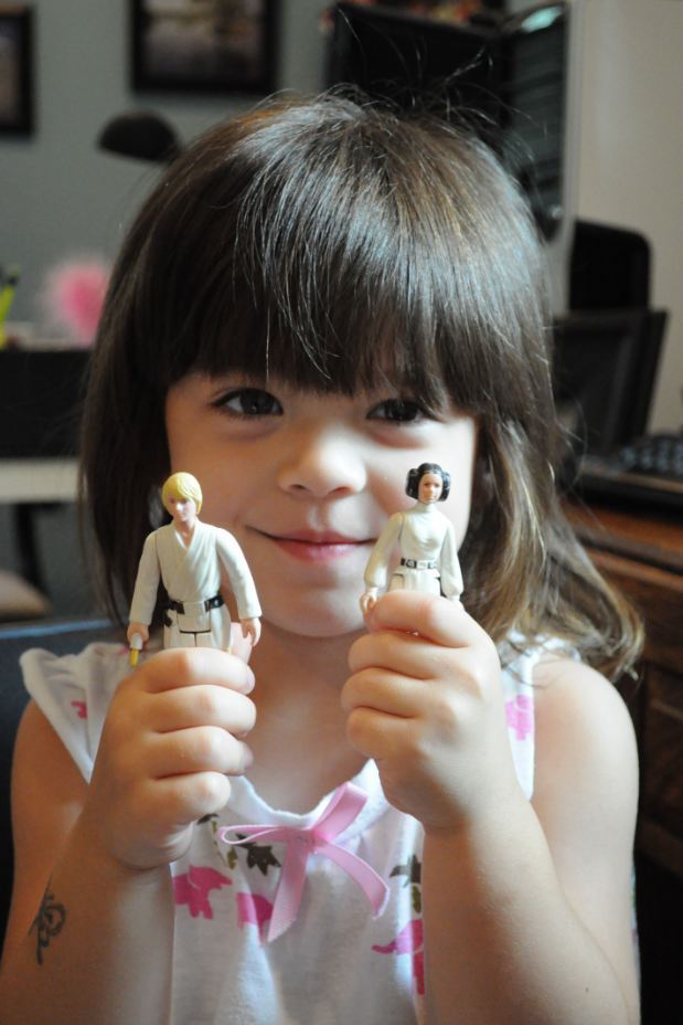 A young girl holds action figures of Luke Skywalker and Princess Leia.