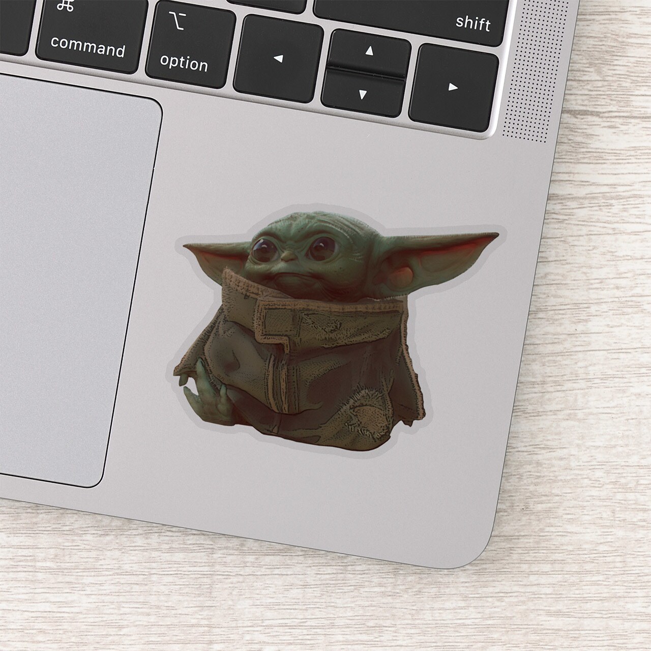 A sticker of Grogu next to the trackpad of a Macbook.