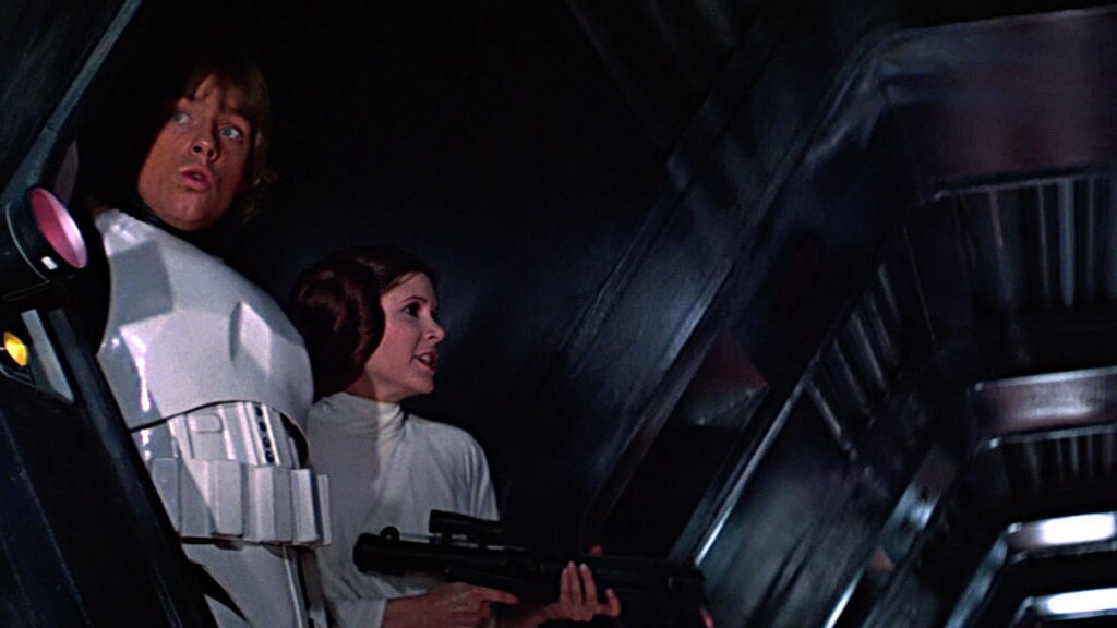 Luke, in stormtrooper armor, stands next to Leia wielding a blaster rifle on the Death Star in A New Hope.