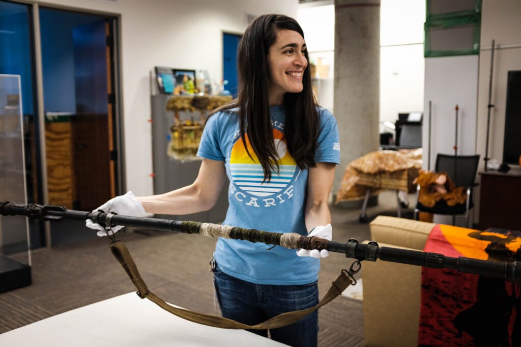 Lucasfilms archivist Madlyn Burkert smiles while holding Rey's staff with gloved hands.
