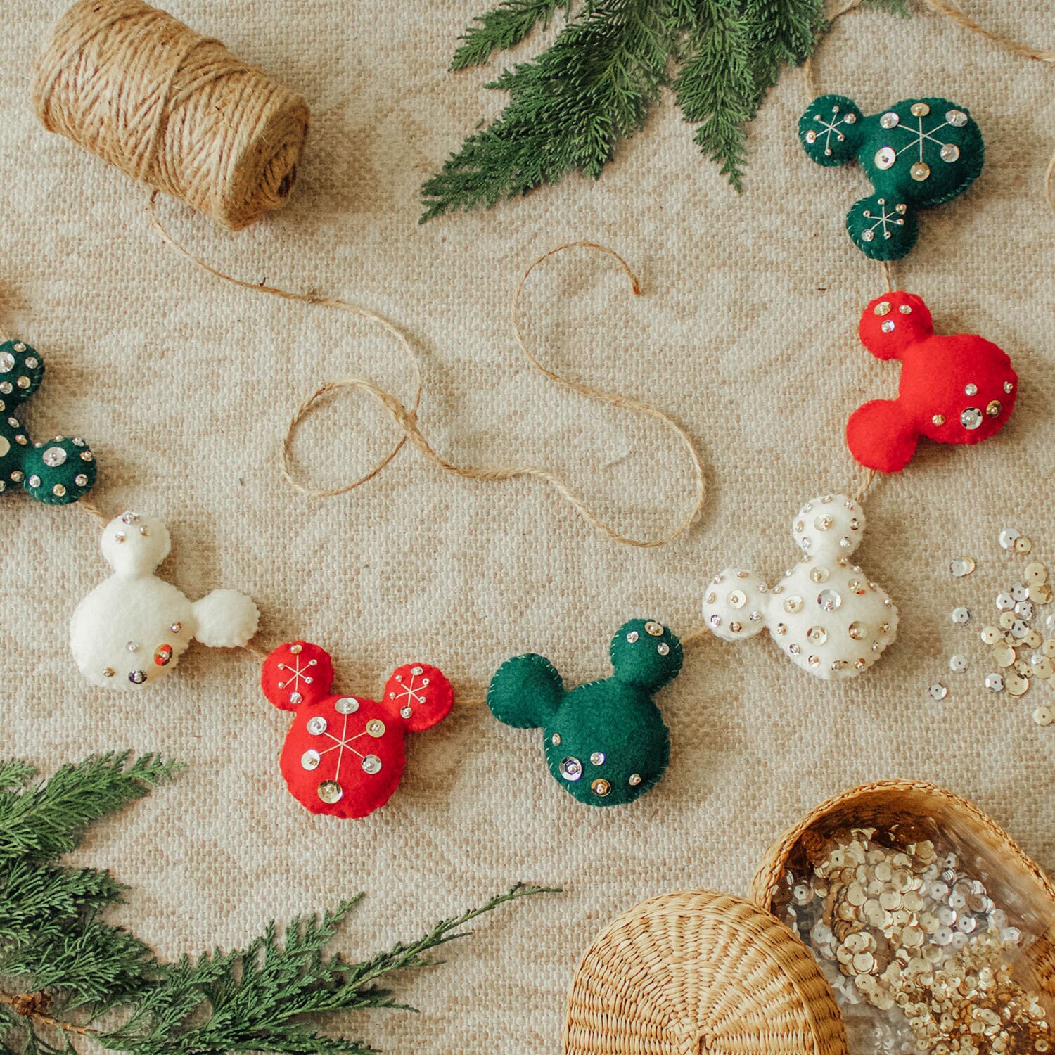 Off-white, red, and green felt Mickey Mouse heads decorated with sequins and beads strung together to form a holiday garland.