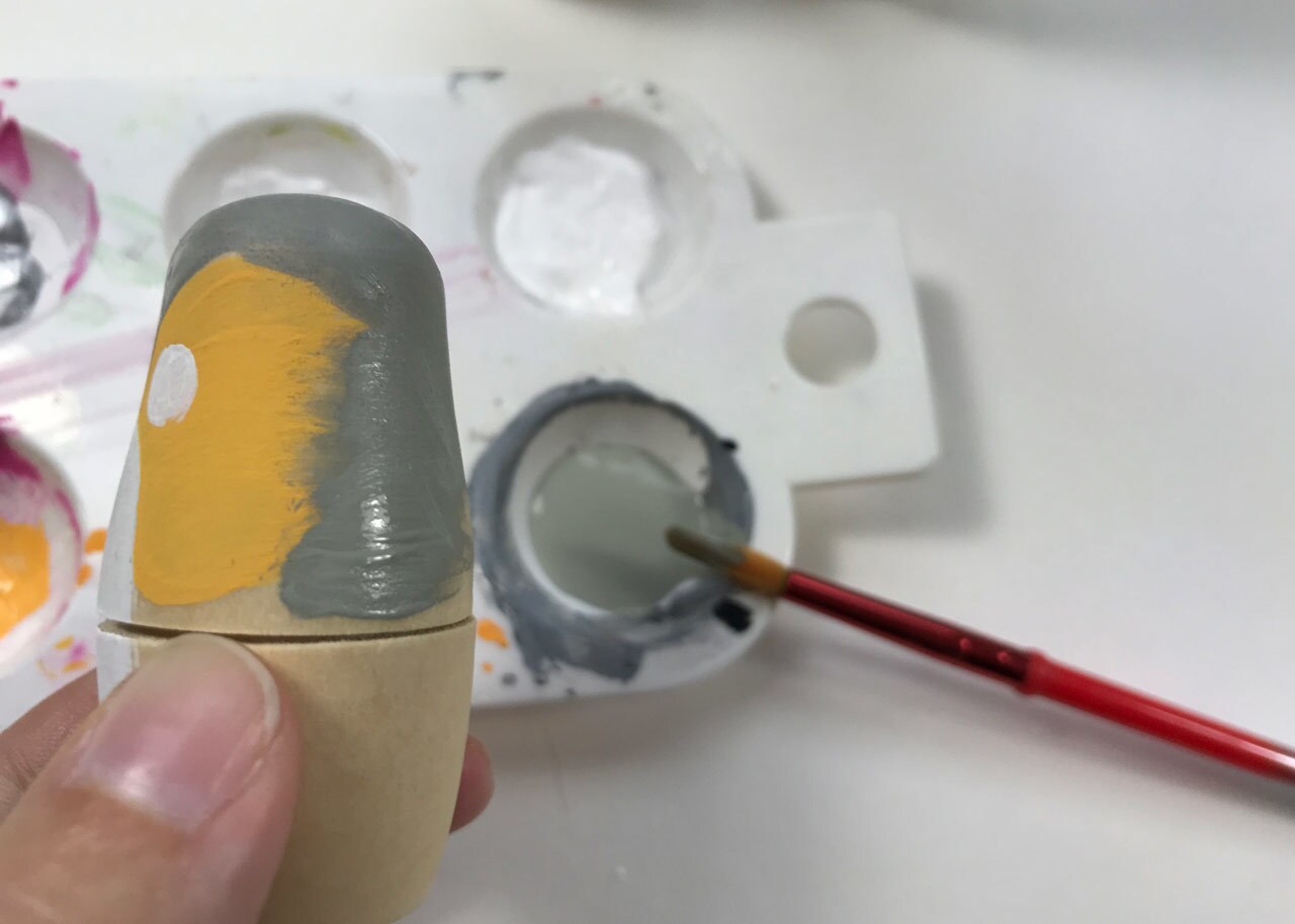 An artist paints a wooden nesting doll to look like a porg.