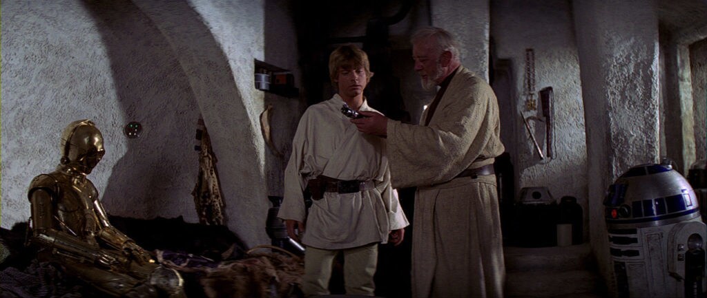 Obi-Wan shows a lightsaber to Luke while C-3PO and R2-D2 rest in A New Hope.