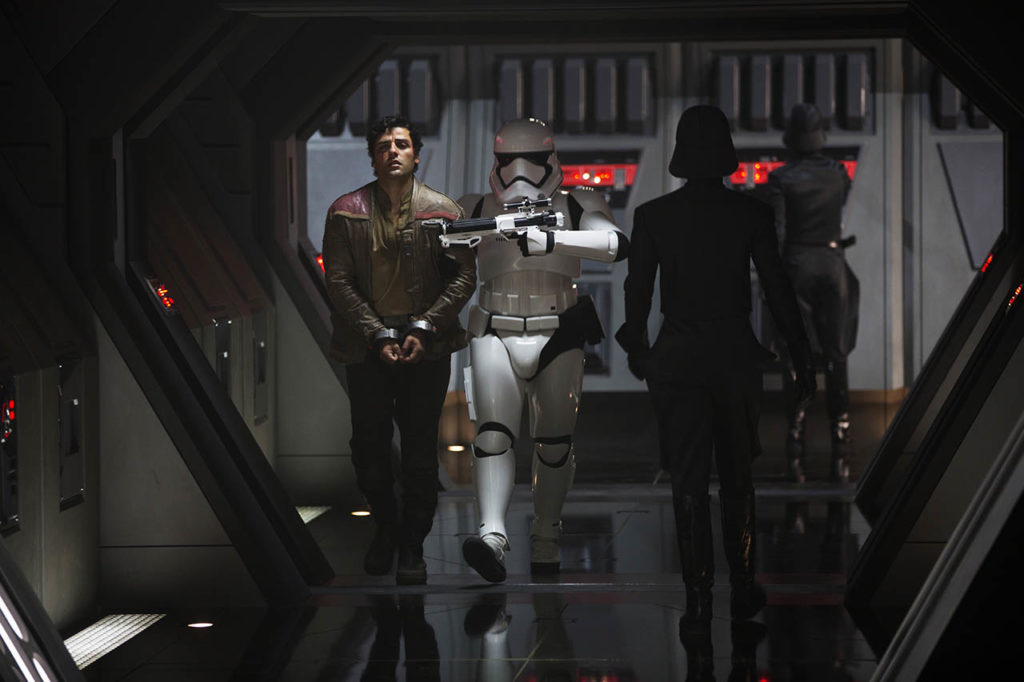 Finn, in stormtrooper armor, escorts Poe down a hallway.
