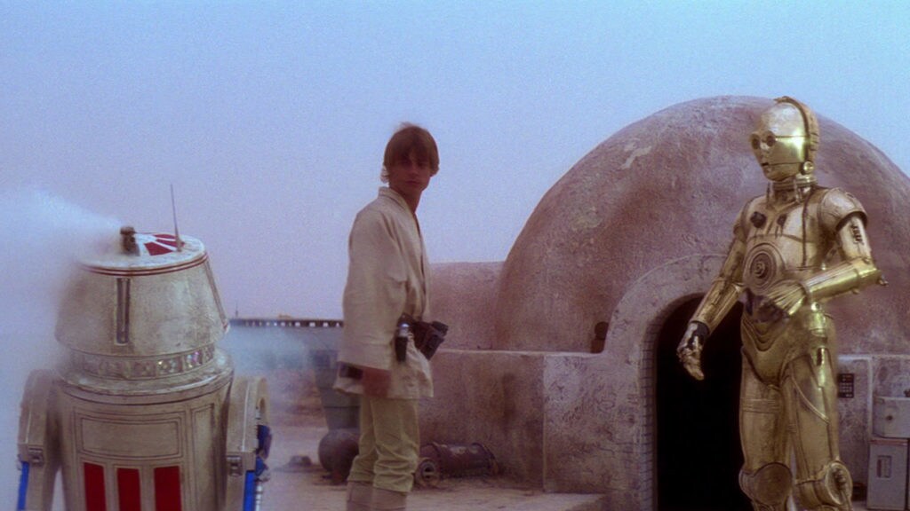 Luke Skywalker and C-3PO look at a broken droid outside Luke's home on Tatooine.