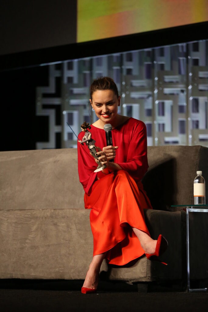 Daisy Ridley holds a microphone and a Rey figurine on stage.