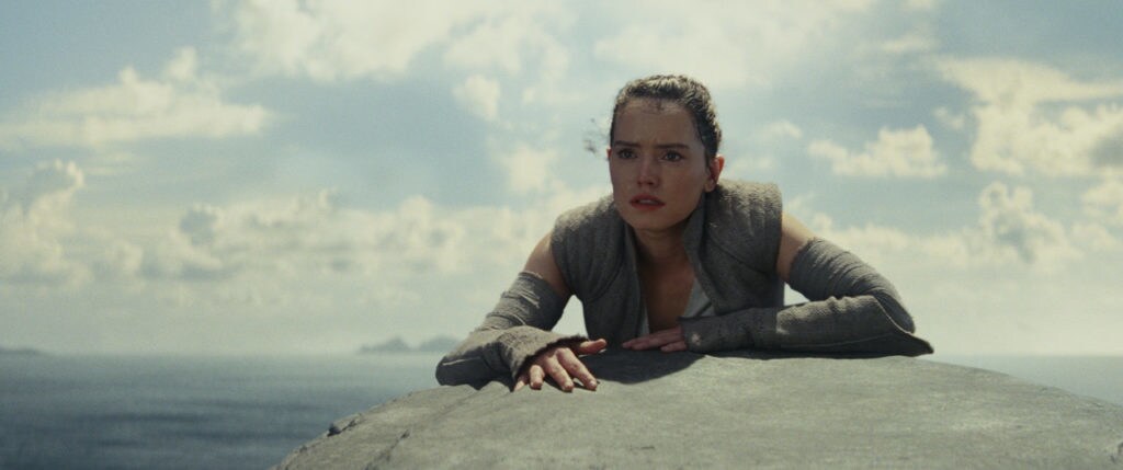 Rey climbs over the edge of a large rock in The Last Jedi.