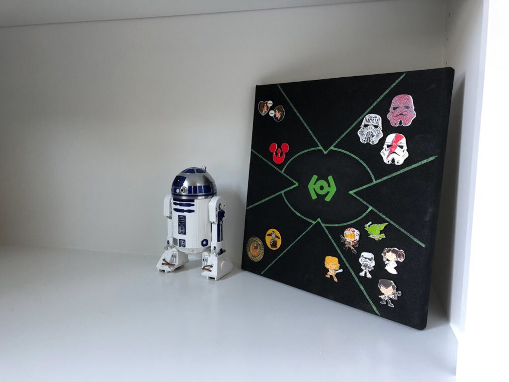 A finished DIY enamel pin board with R2-D2 standing next to it.