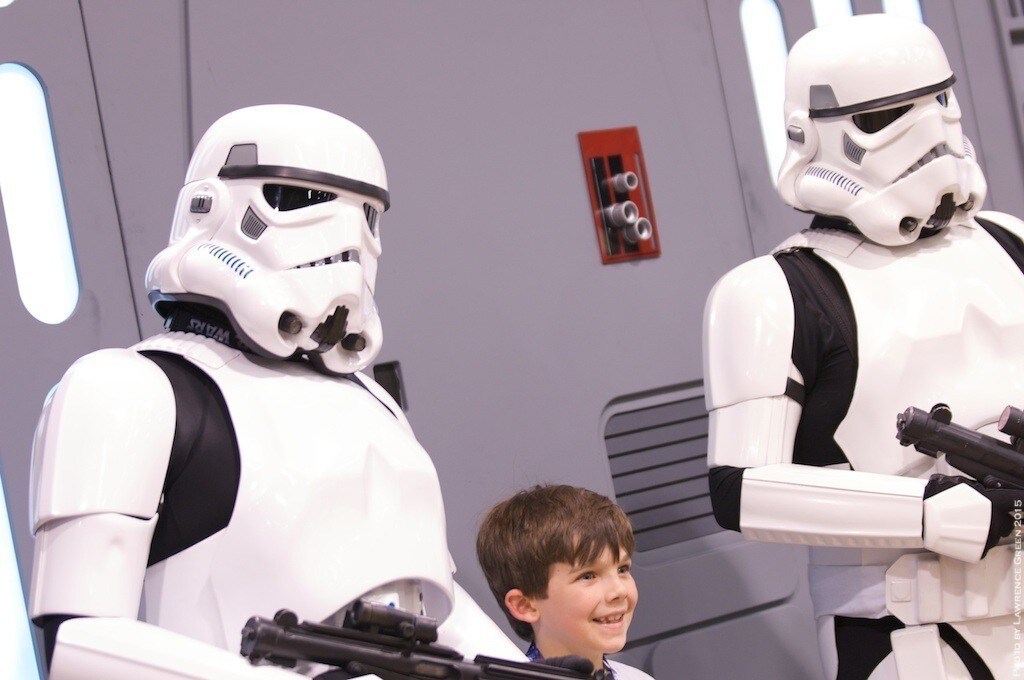 Two cosplayers dressed as stormtroopers pose for a photo with a small child at a Star Wars Celebration event.