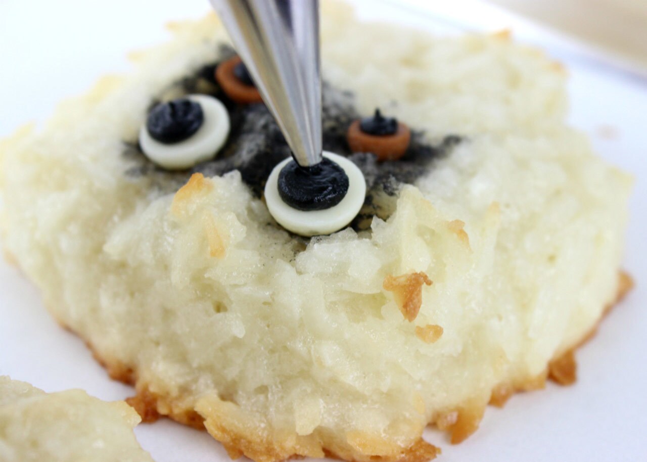 Black icing is piped onto white chocolate chips to create the look of pupils for the eyes on a Muftak Macaroon.