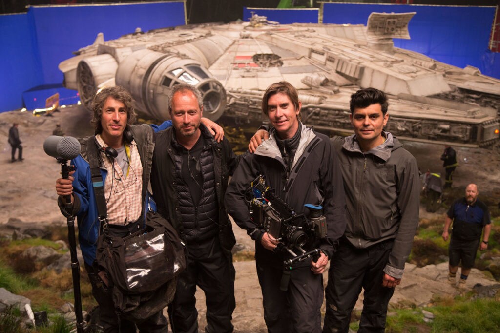 Documentary film crew Andy Yarme, Anthony Wonke, Neil Harvey, and Ariel Grandoli stand on the set of The Last Jedi with the Millennium Falcon behind them.
