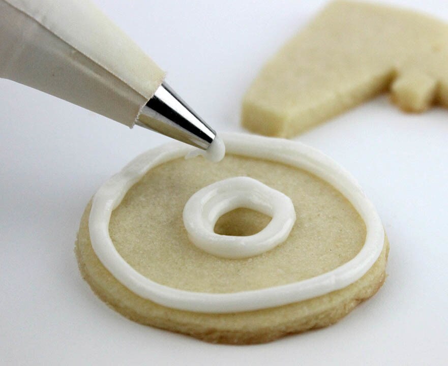 White icing is piped onto the wheel of a D-O cookie.