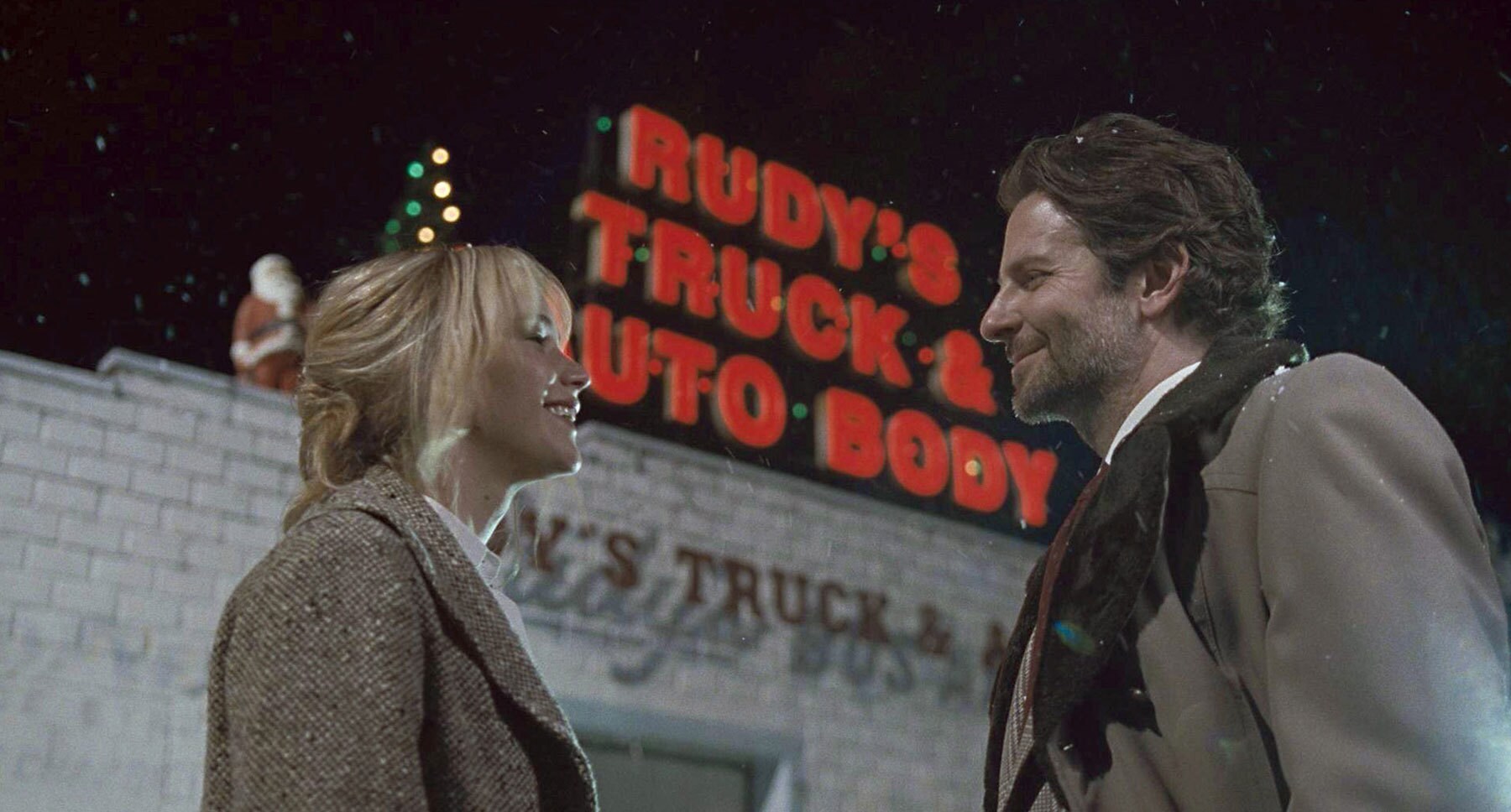 Bradley Cooper (as Neil Walker) and Jennifer Lawrence (as Joy) standing outside of Rudy's Audo Shop in "Joy"