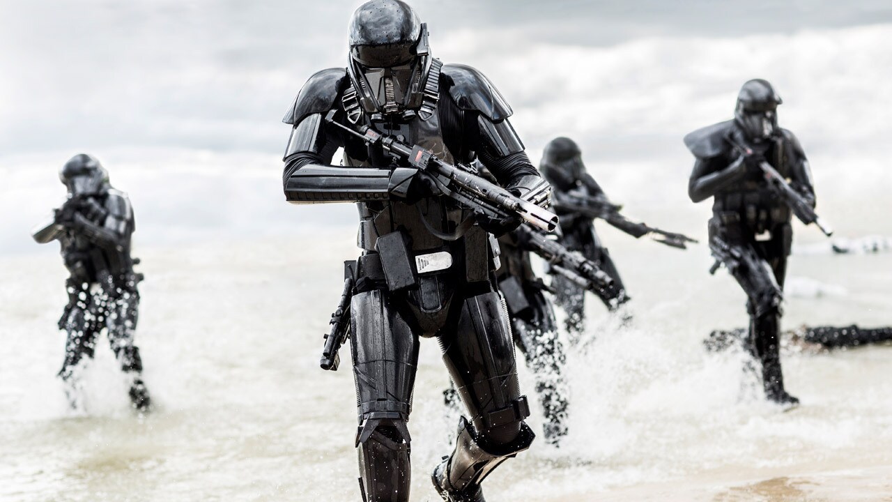 Death troopers wield blaster rifles while running through a shoreline in Rogue One.