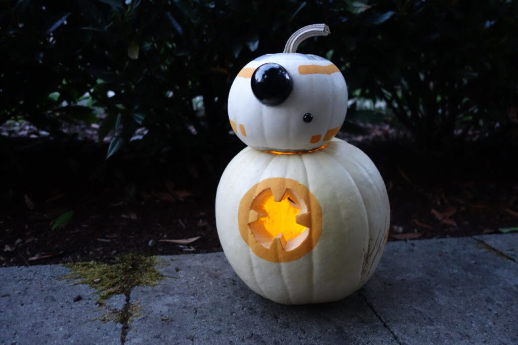 A BB-8 jack-o-lantern made of two white pumpkins stacked on top of each other, carved and decorated with orange and silver paint.