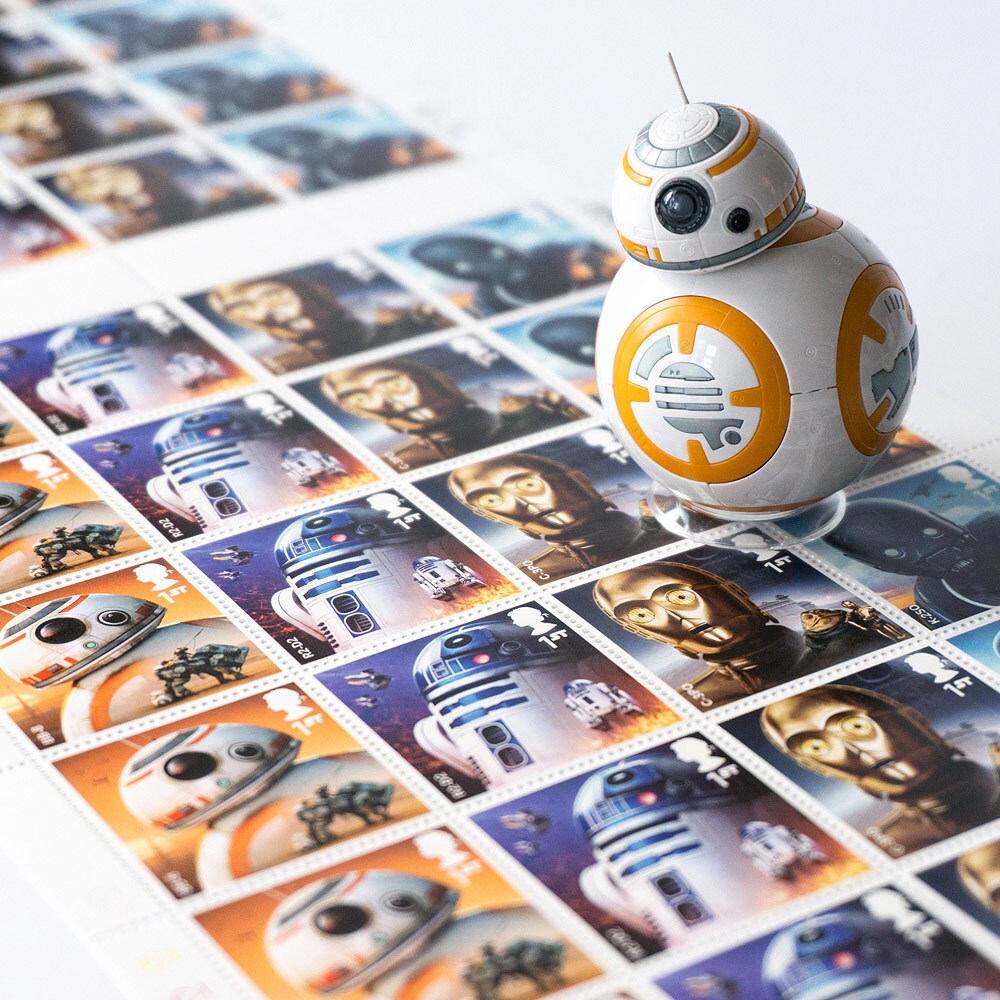 A BB-8 action figure on top of a sheet of Royal Mail postage stamps depicting BB-8, R2-D2, C-3PO, and K-2SO.