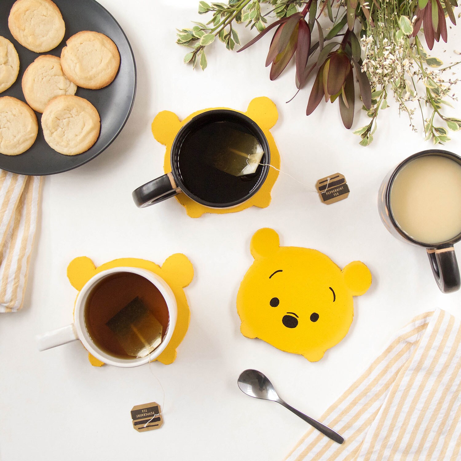 Several coasters decorated like Winnie the Pooh on a table with mugs and cookies.