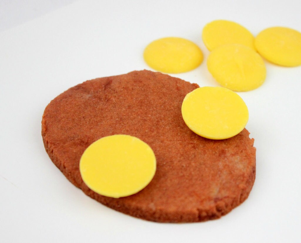 Yellow candy melts are placed on both sides of an oval cookie to create eyes.