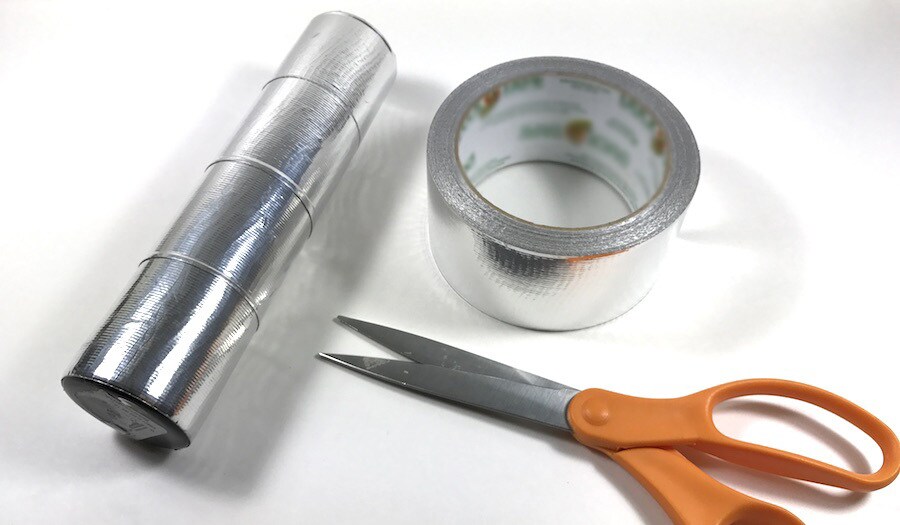 A vase partially wrapped wrapped in duct tape to resemble a lightsaber, next to scissors and a roll of silver duct tape.
