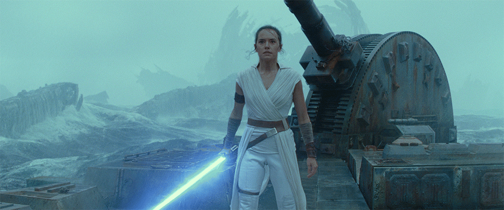 Rey stands on the wreckage of the second Death Star while holding a lightsaber, in a GIF.