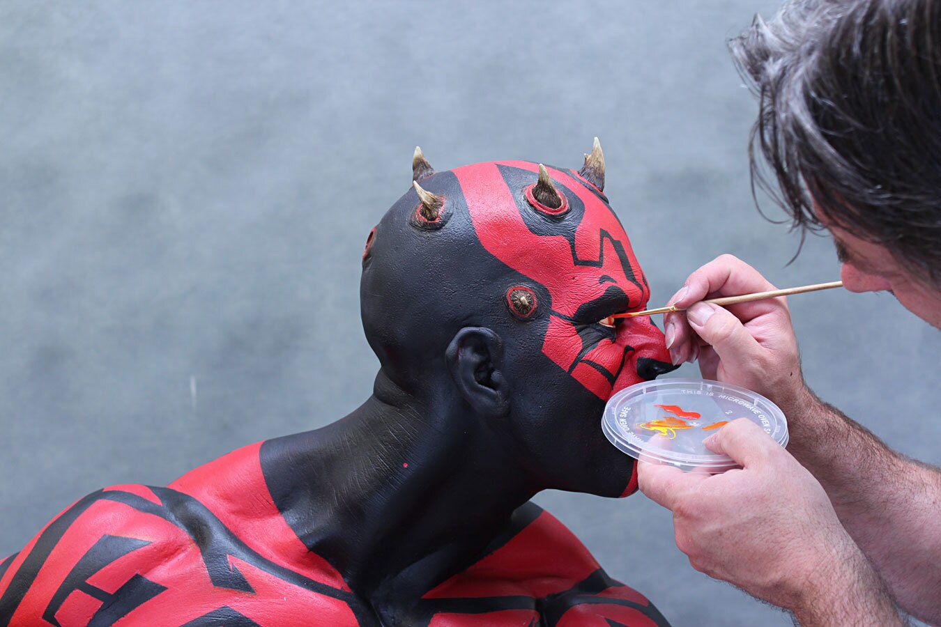 A man paints eyes onto a life-sized bust of Darth Maul.