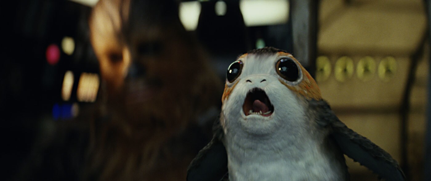A porg screams in the cockpit of the Millennium Falcon with Chewbacca in the background.
