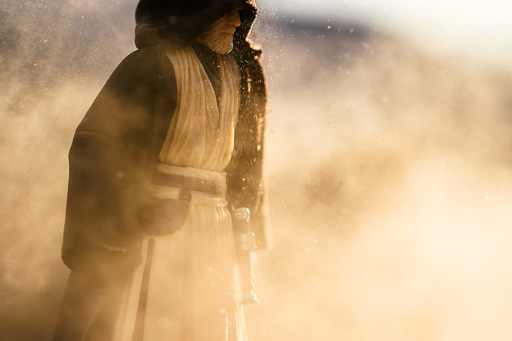 A cloaked Obi-Wan Kenobi action figure, posed in a simulated sandstorm.