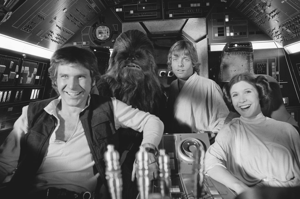 Han Solo, Chewbacca, Luke Skywalker, and Princess Leia laughing in the cockpit of the Millennium Falcon in Star Wars: A New Hope.