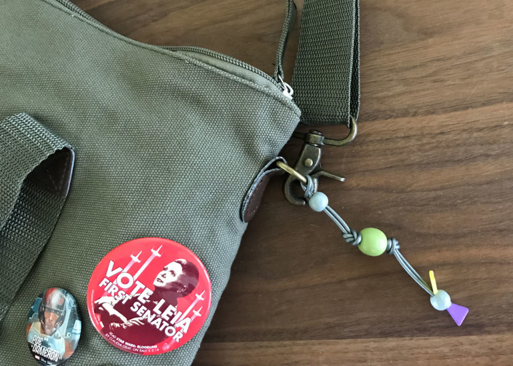 Homemade silka beads hang off a messenger bag adorned with Star Wars pins.