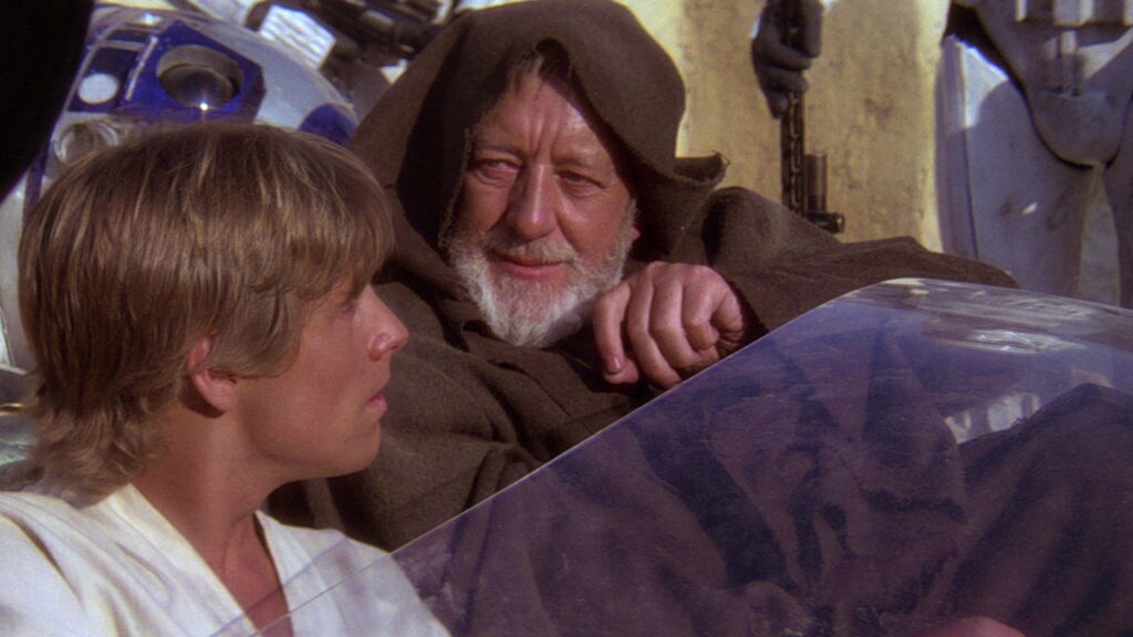 Obi-Wan Kenobi and Luke Skywalker ride into Mos Eisley on a landspeeder with R2-D2 in the back.