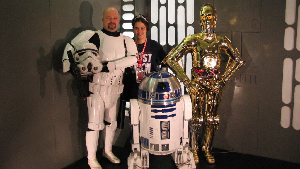 Albin Johnson, founder of the 501st Legion costuming organization, cosplays in stormtrooper armor while standing next to his wife, R2-D2, and C-3PO.