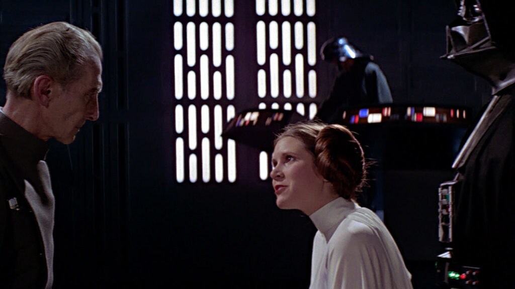 Princess Leia speaks to Grand Moff Tarkin while Darth Vader stands behind her in A New Hope.