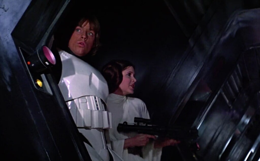 Luke, in stormtrooper armor, stands beside Leia wielding a blaster rifle in A New Hope.