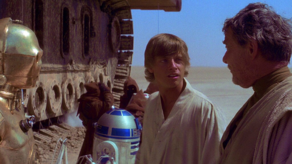 Luke talks to his uncle Owen with C-3PO standing next them and R2-D2 and Jawas in the background in front of a sandcrawler in A New Hope.