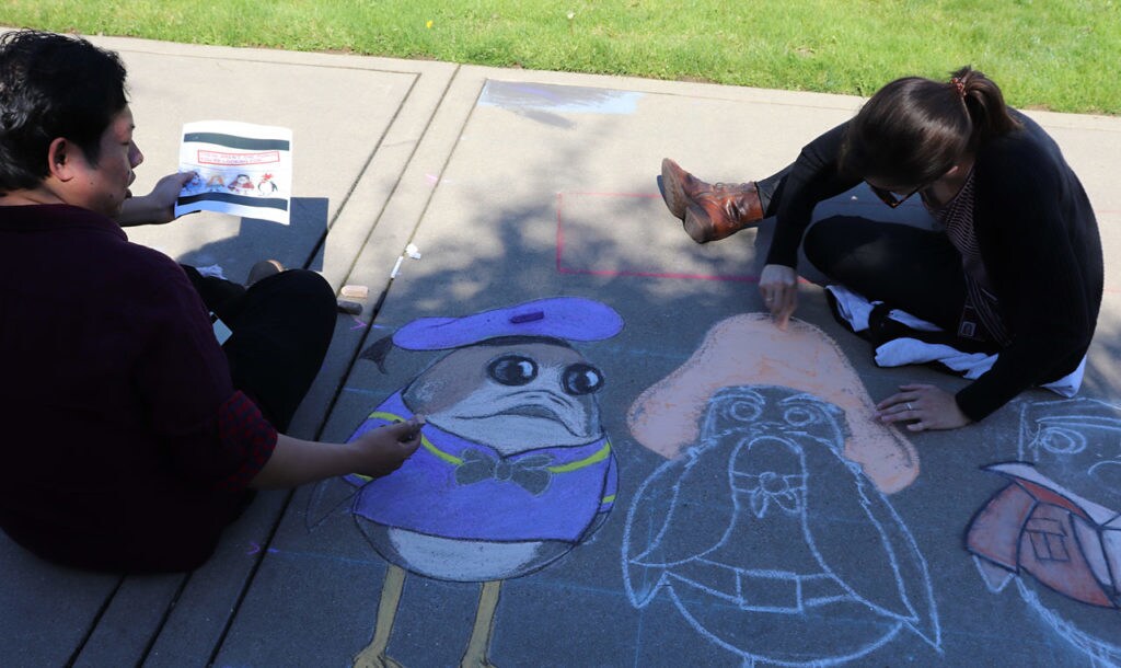 Artists work on chalk illustrations of porgs in a sailor costume and a wild west outfit.