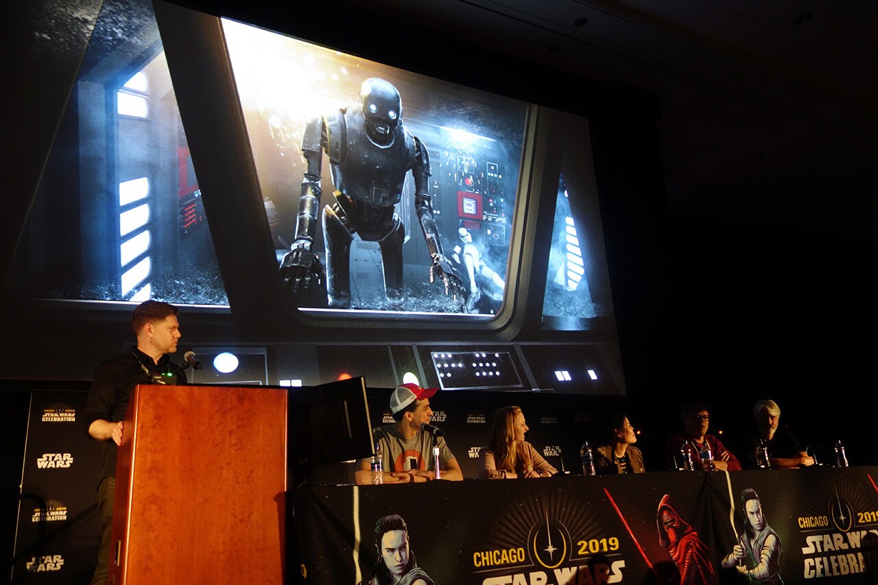ILMxLAB panelists speak at the Chicago 2019 Star Wars Celebration. Behind them, a projector features an image of K-2SO.