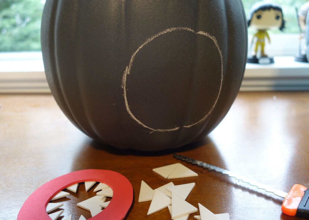 A painted pumpkin sits on a table next to a carving knife and craft foam.