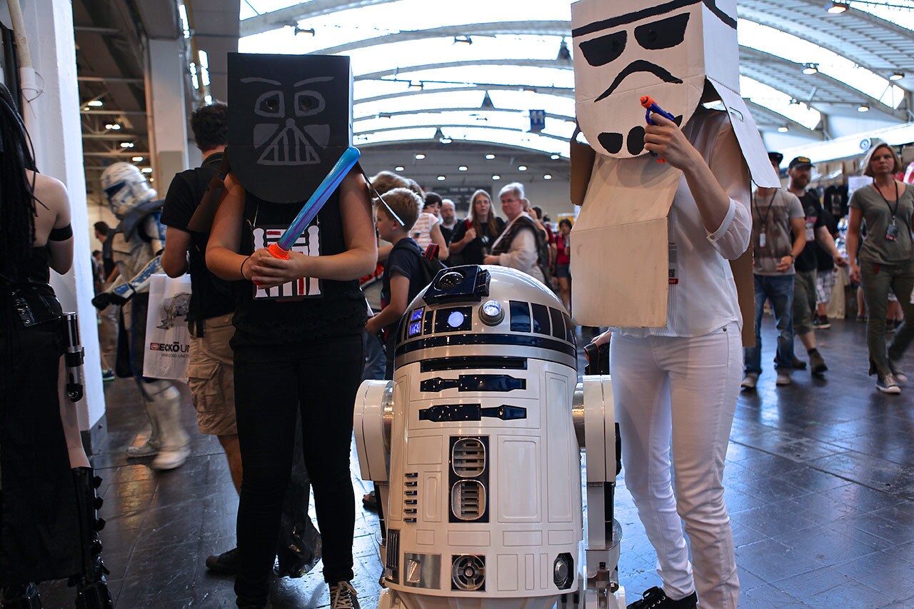 A Darth Vader cosplayer and a stormtrooper cosplayer stand on either side of R2-D2.